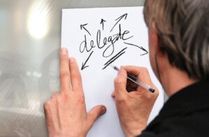 Man writing the word "delegate" on paper.