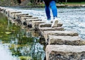 A person walking on stones across a river.